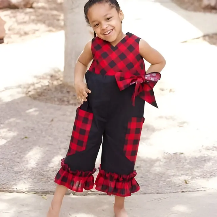 Child in red plaid outfit smiling outdoors.