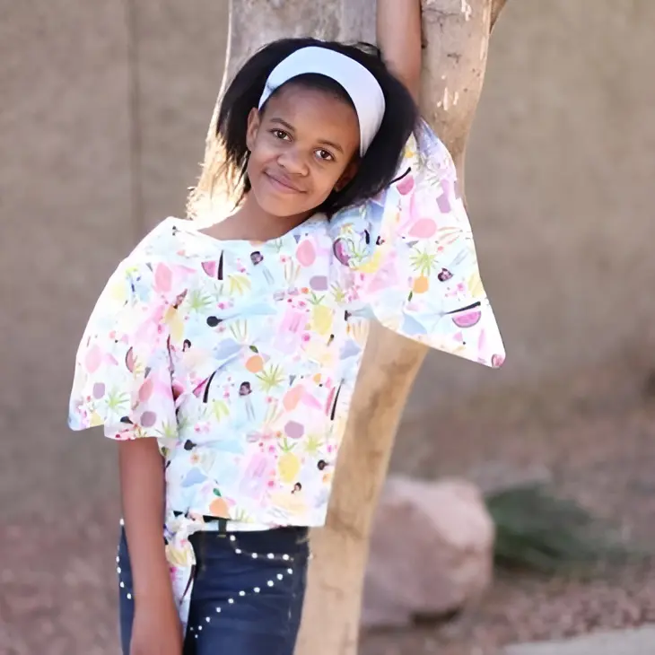 Girl leaning on tree, wearing colorful shirt.