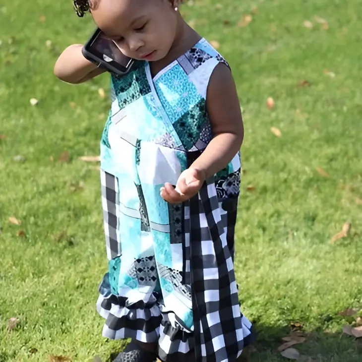 Toddler in colorful dress using cellphone.