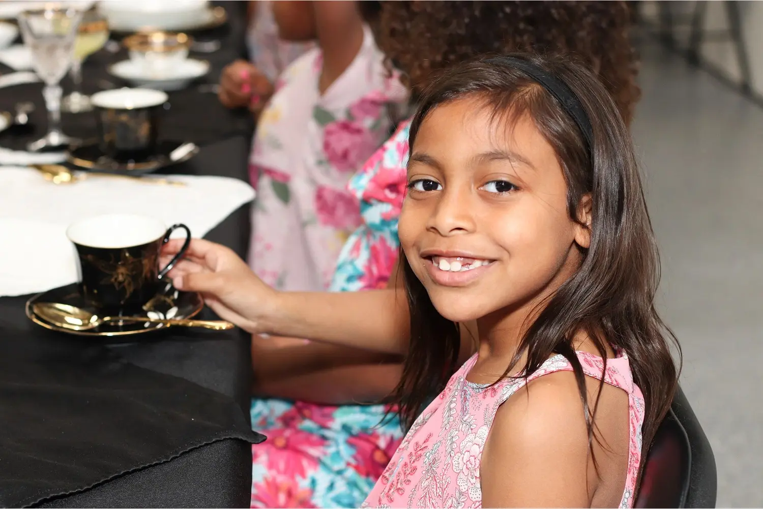 Girl smiling, holding teacup, at table.