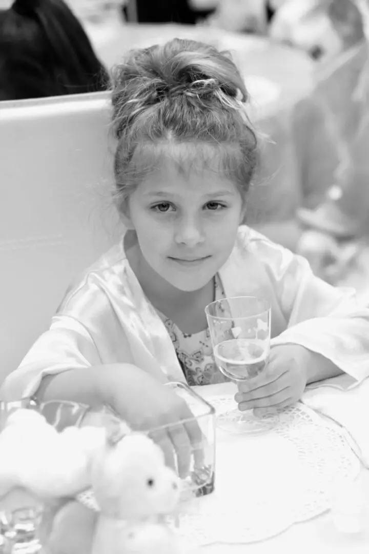 Girl holding a glass at a table.