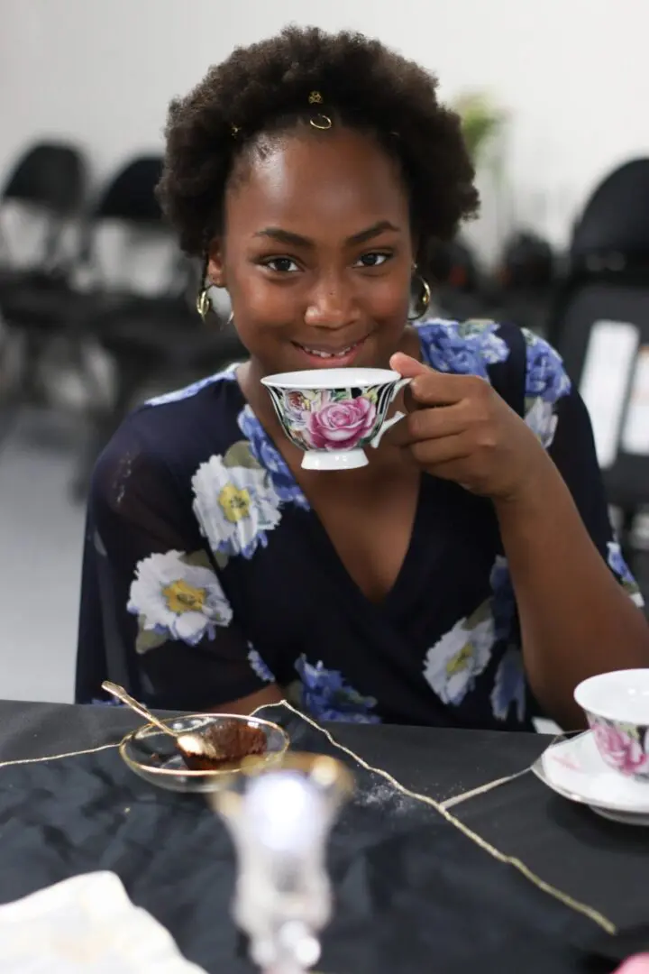 Woman smiling, holding floral teacup at table.