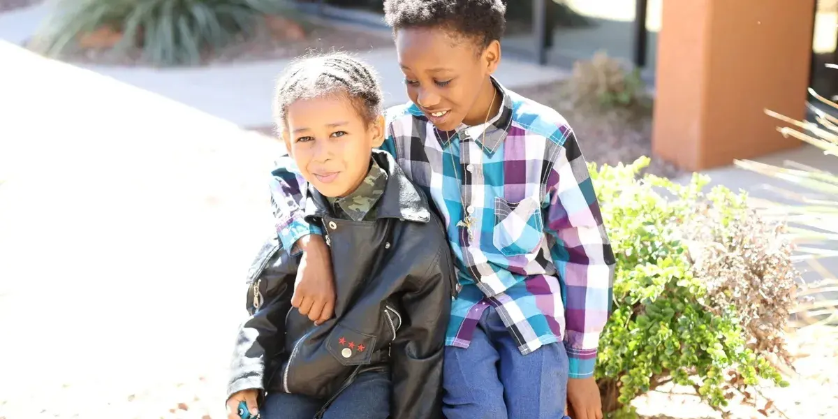 Two children sitting outside, smiling together.