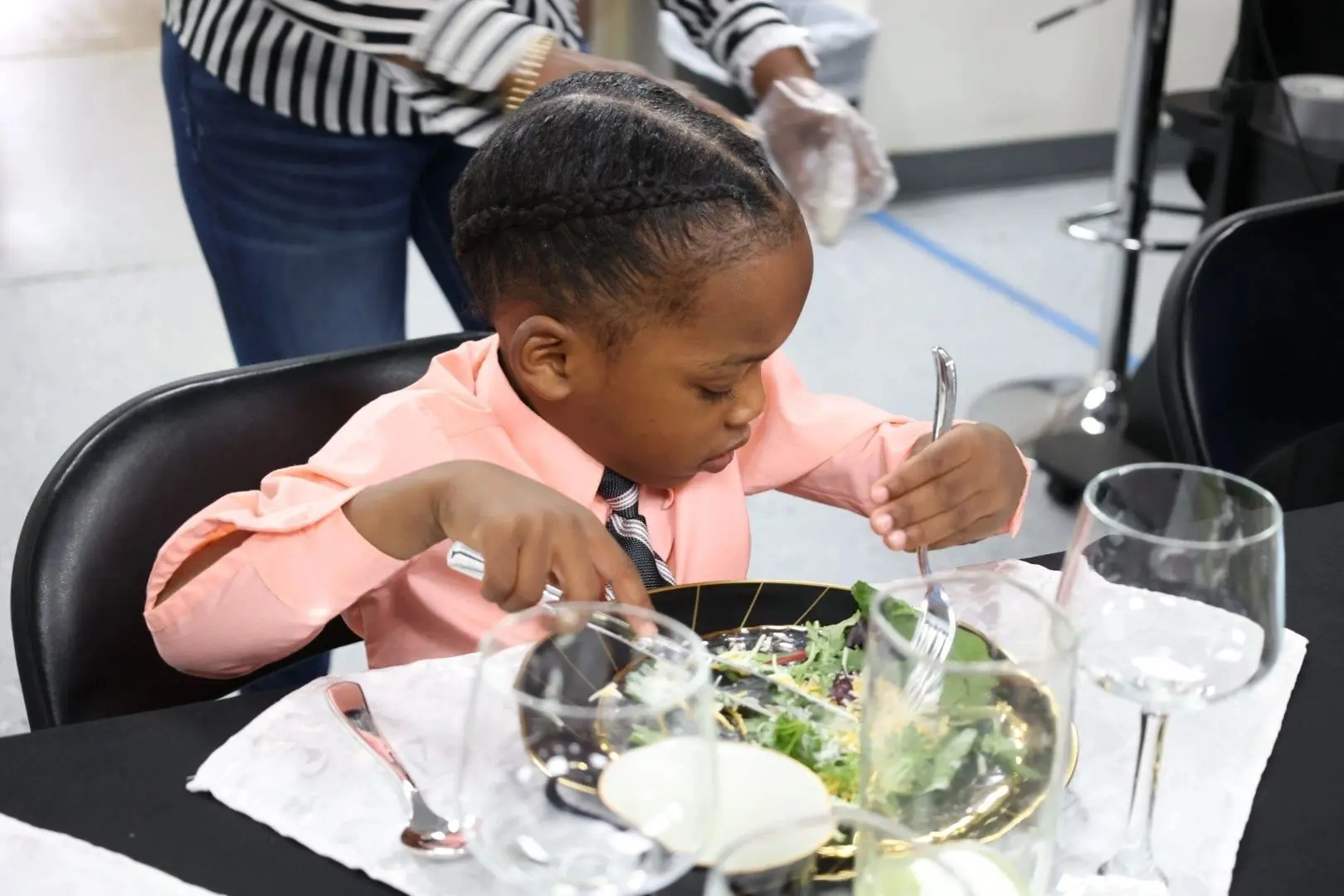 Child eating salad at a dining table.