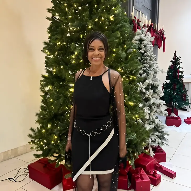 Woman smiling beside decorated Christmas tree indoors.