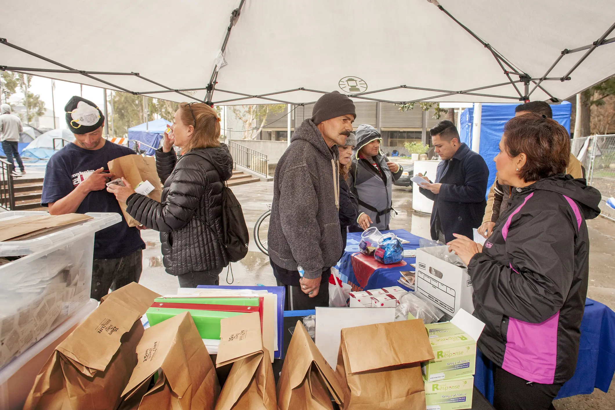 People shopping at an outdoor market stall with various goods.