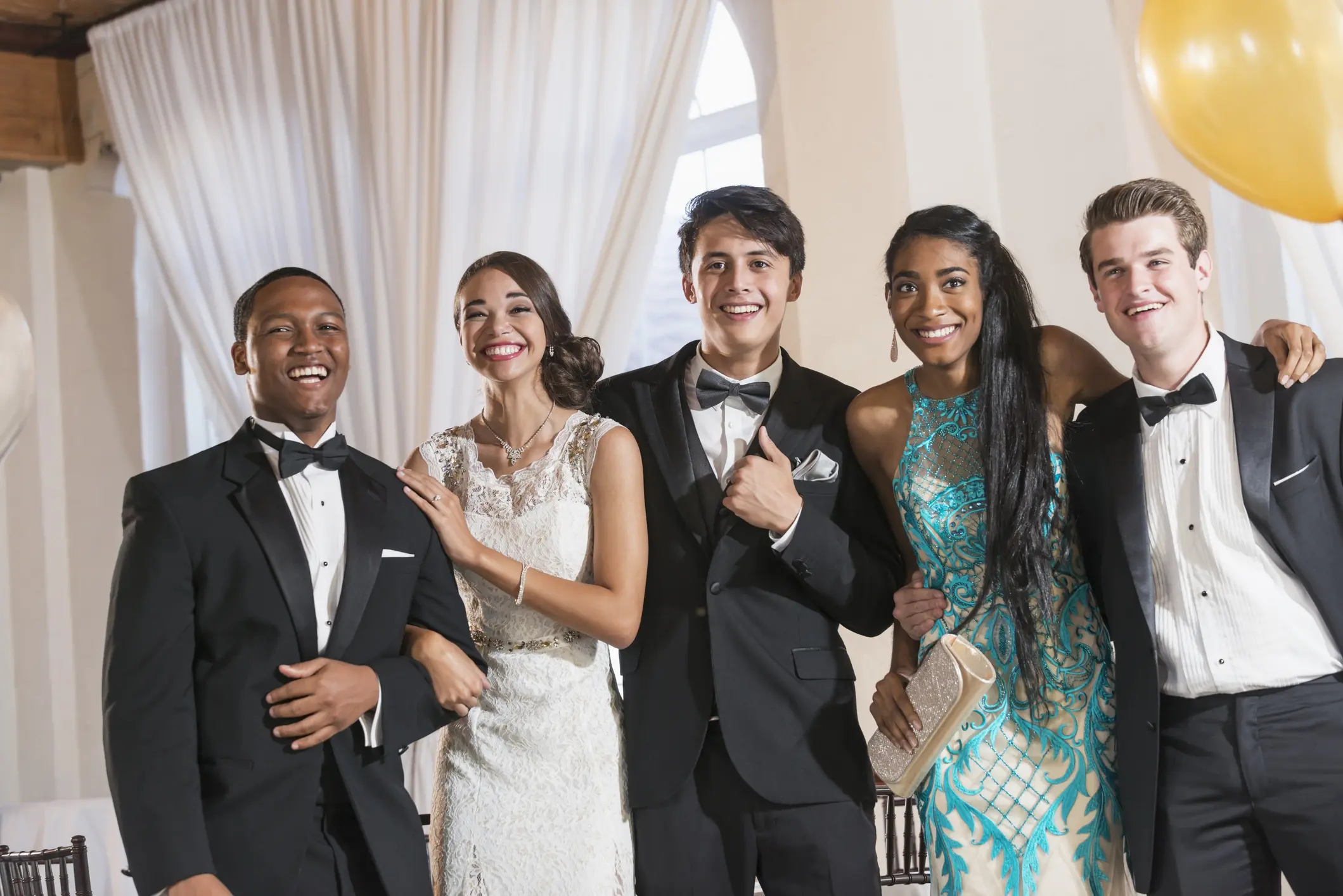 A group of five friends dressed up, smiling at a formal event.
